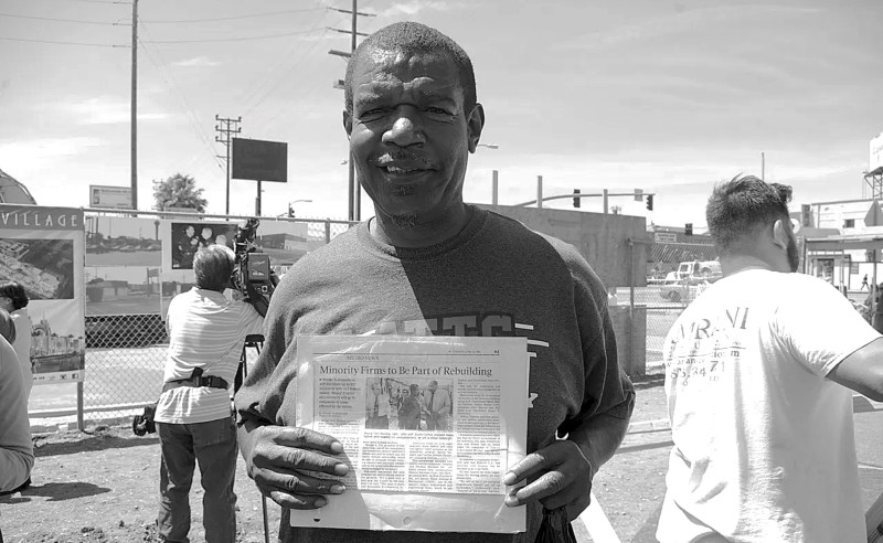 At yesterday's groundbreaking at Manchester and Vermont, South L.A. resident Dana Gilbert holds an L.A. Times article from 1992 about the plans to rebuild South L.A. using minority contractors. The article features a photo of himself with then-Mayor Tom Bradley standing in the Manchester/Vermont lot. Gilbert showed up to ask for the jobs he and other residents were promised 23 years ago. Sahra Sulaiman/Streetsblog L.A.