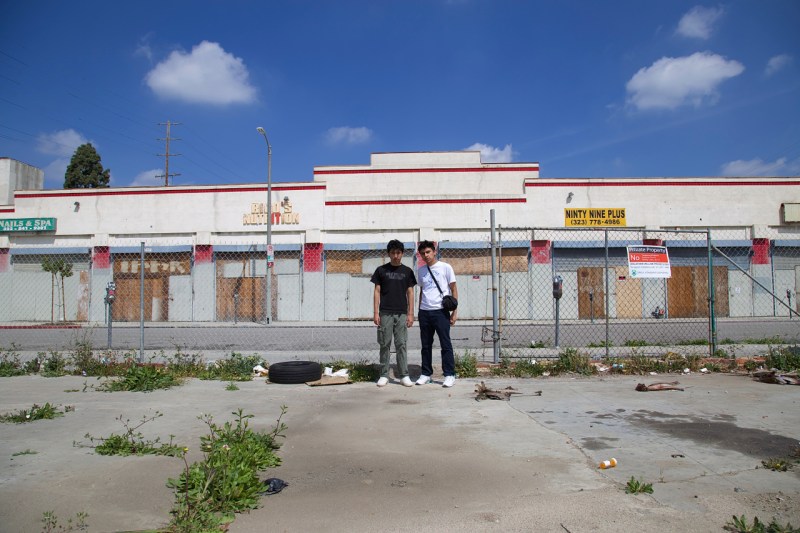 Juan Carlos Mercado and Miguel Sanchez stand in a vacant lot at Manchester and Vermont. The former swap meet site saw a groundbreaking three years ago but the mall project, planned by developer Eli Sasson, never materialized. And the buildings behind the youth - occupied by homeless folks from the area - burned down in February. Sahra Sulaiman/Streetsblog L.A.