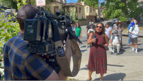 Ananya Roy, Director of the Luskin Institute on Inequality and Democracy at UCLA, speaks for the cameras. In the background is an abandoned property owned by Caltrans.