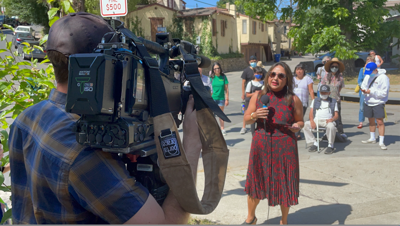 Ananya Roy, Director of the Luskin Institute on Inequality and Democracy at UCLA, speaks for the cameras. In the background is an abandoned property owned by Caltrans.